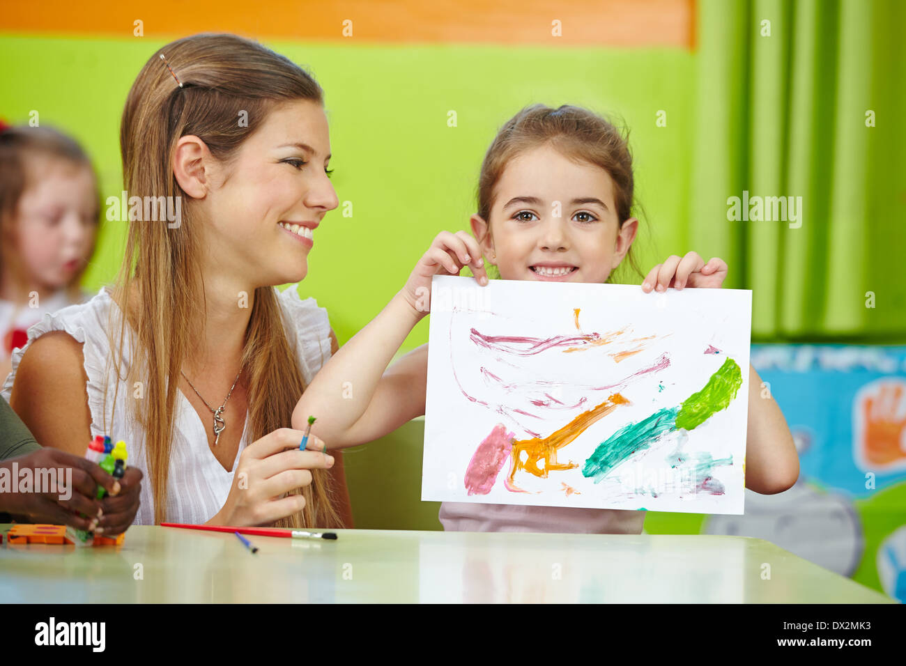 Mädchen zeigen selbst gezeichnet mit Kindergärtnerin im Kindergarten malen Stockfoto