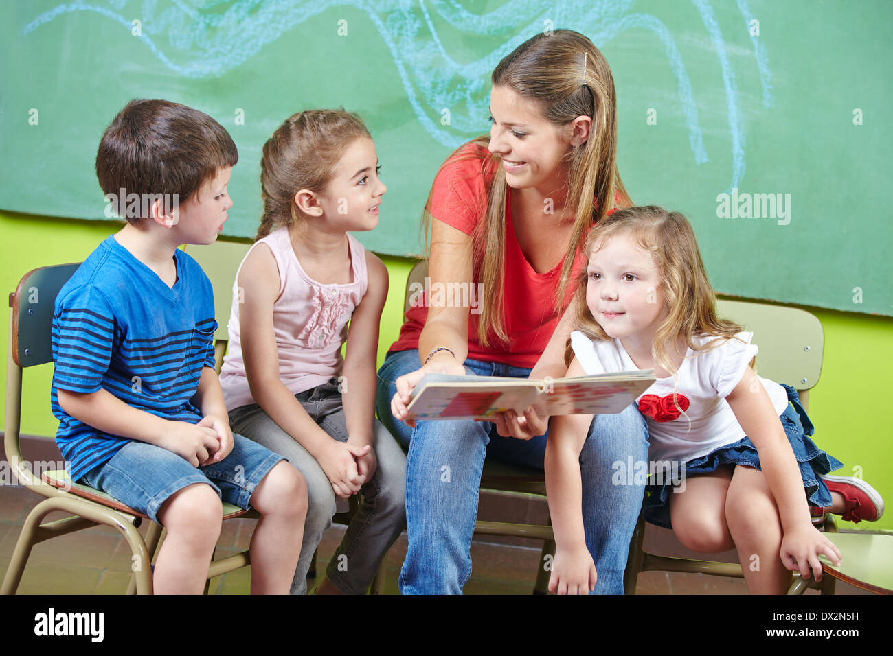 Kind-Pflegedienst und Kinder lesen ein Bilderbuch zusammen in einem kindergarten Stockfoto