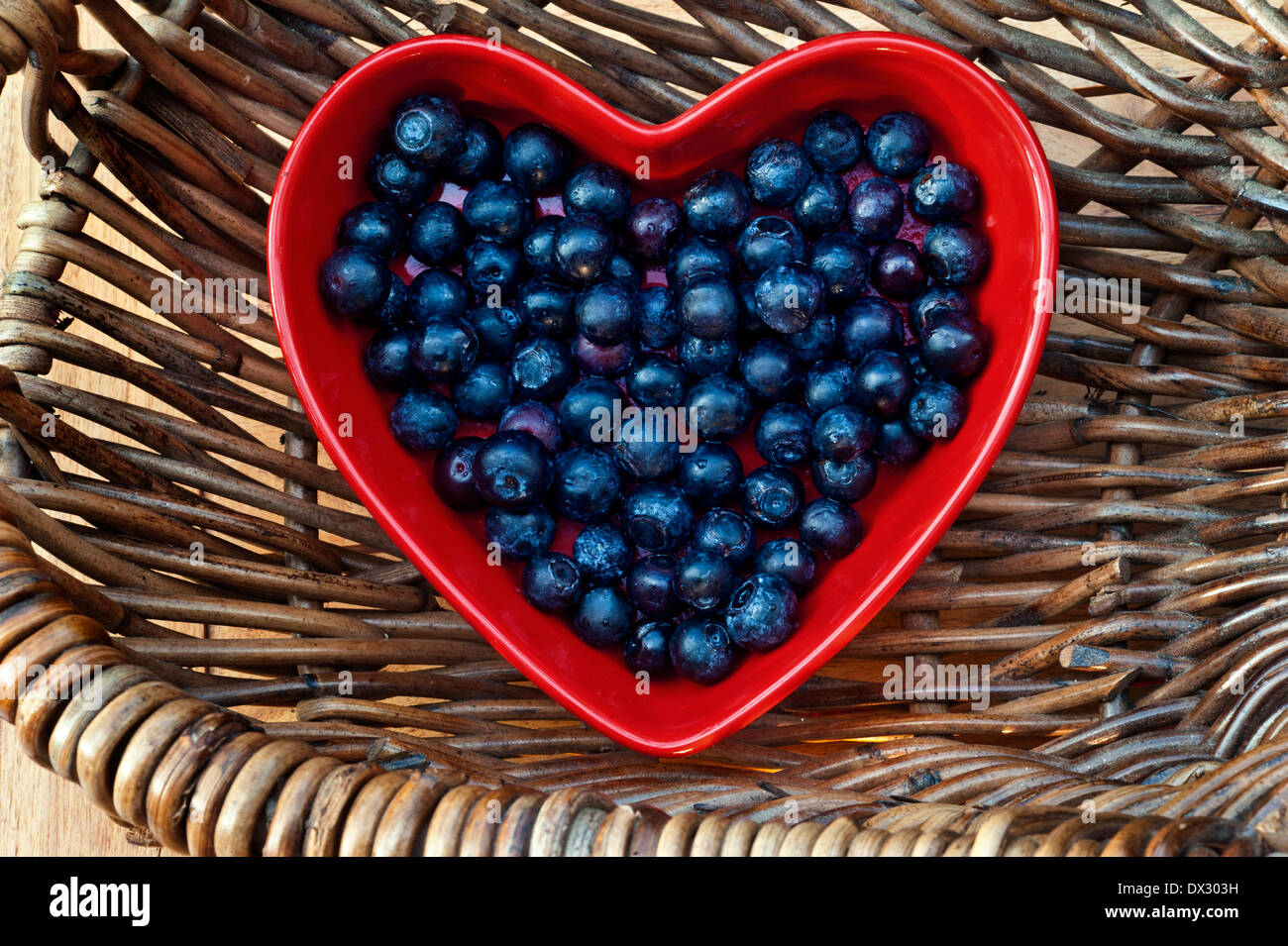 Heidelbeeren Herz gesundes Herz Konzept/Blaubeeren in einem roten herzförmigen Gericht, das in einem traditionellen Weidenkorb Stockfoto