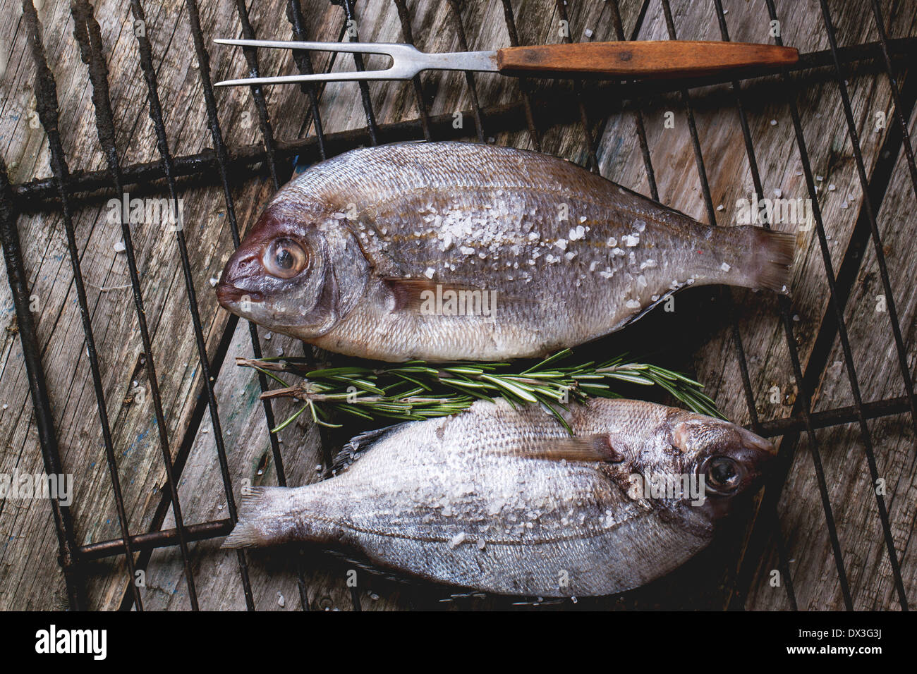 Draufsicht auf Schlepptau Rohfisch Brassen mit Rosmarin und Meer Salz auf Grill über alten Holztisch. Stockfoto
