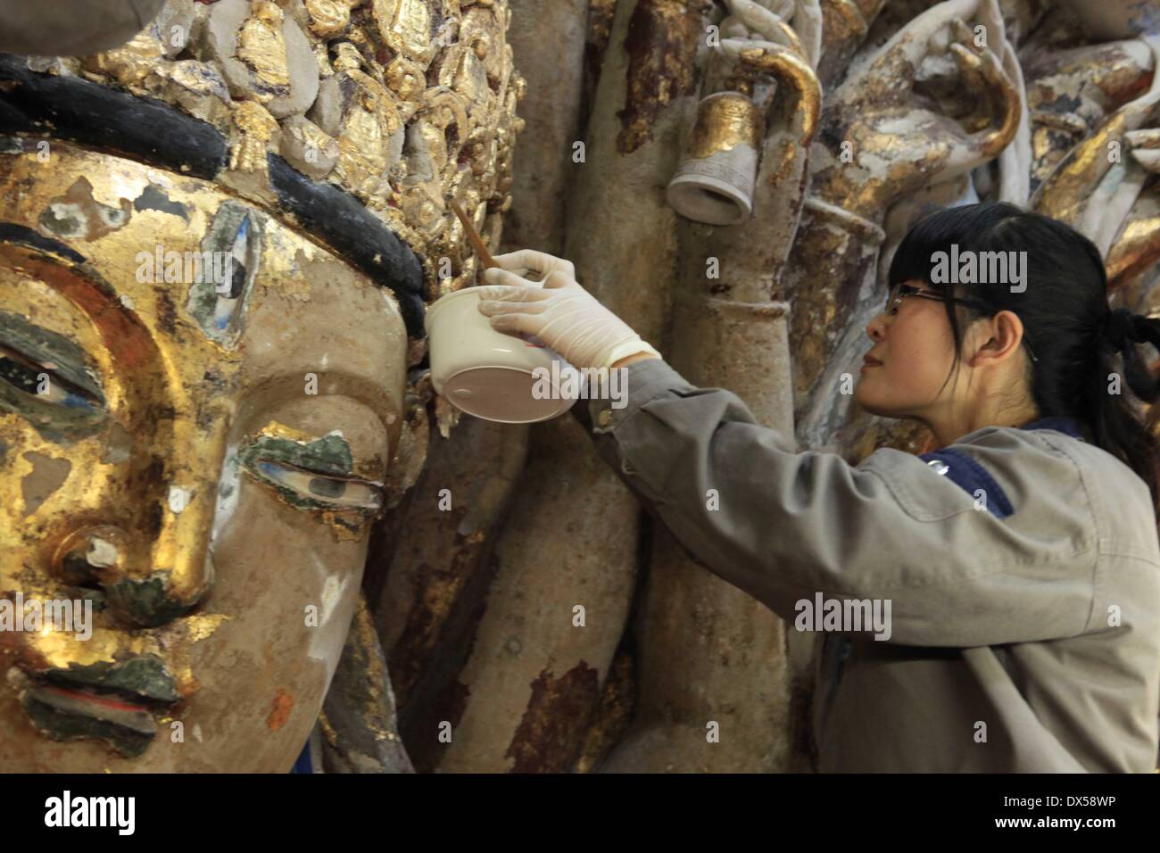 (140318)--CHONGQING, 18. März 2014 (Xinhua)--A Personal Mitglied löscht peeling Goldfolie aus der Skulptur Qianshou Guanyin (Bodhisattva mit tausend Händen) auf Mount Baoding im Bezirk Dazu in der Gemeinde von Chongqing, Südwest-China, 18. März 2014. Die Skulptur geschnitzt in der Höhle mit 7,7 Meter hoch und 12,5 Meter breit, könnte südlichen Song-Dynastie (1127 bis 1279) stammen. Im Laufe der Jahrhunderte die Skulptur Farbe ist verblasst, Teile der Goldfolie Verkleidung haben abgeschält und Risse aufgetreten. Und so wurde ein Restaurierungsprojekt für die buddhistische Statue launche Stockfoto