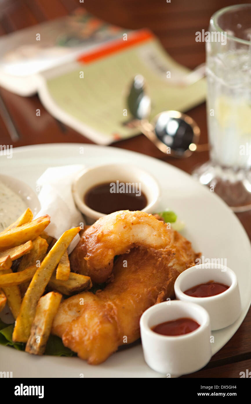 Fish &amp; Chips neben Buch- und Sonnenbrillen am Tisch im Restaurant, Nahaufnahme, hoher Winkel Stockfoto