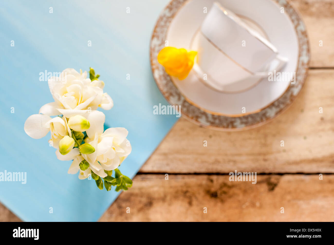 Weißen Freesien auf blauen Matte am rustikalen Holztisch mit unscharfen Vintage Teetasse und gelben Freesien im Hintergrund Stockfoto