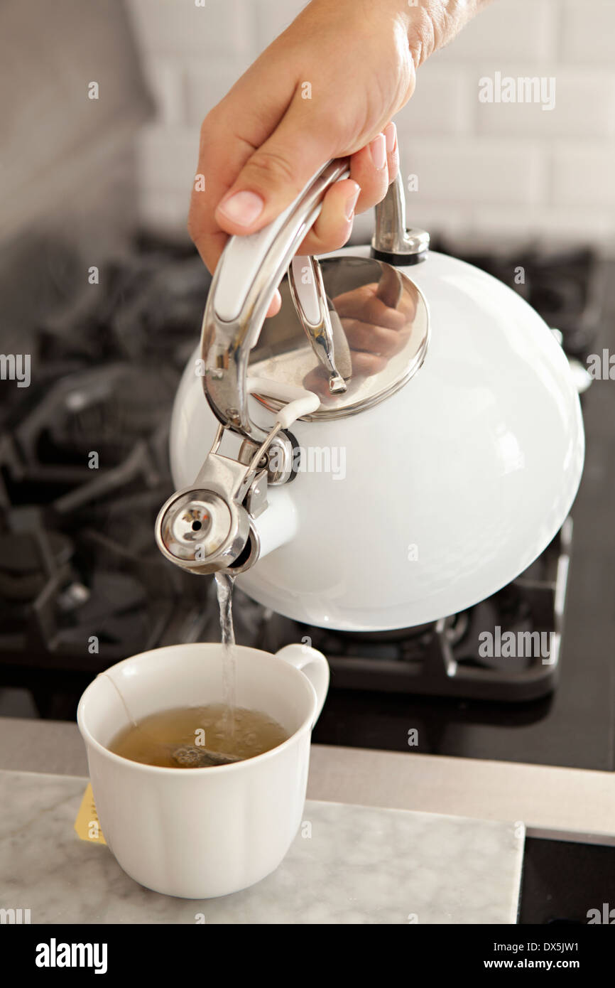 Man gießt heißen Tee aus Wasserkocher in Teetasse in der heimischen Küche, erhöhte Ansicht Stockfoto