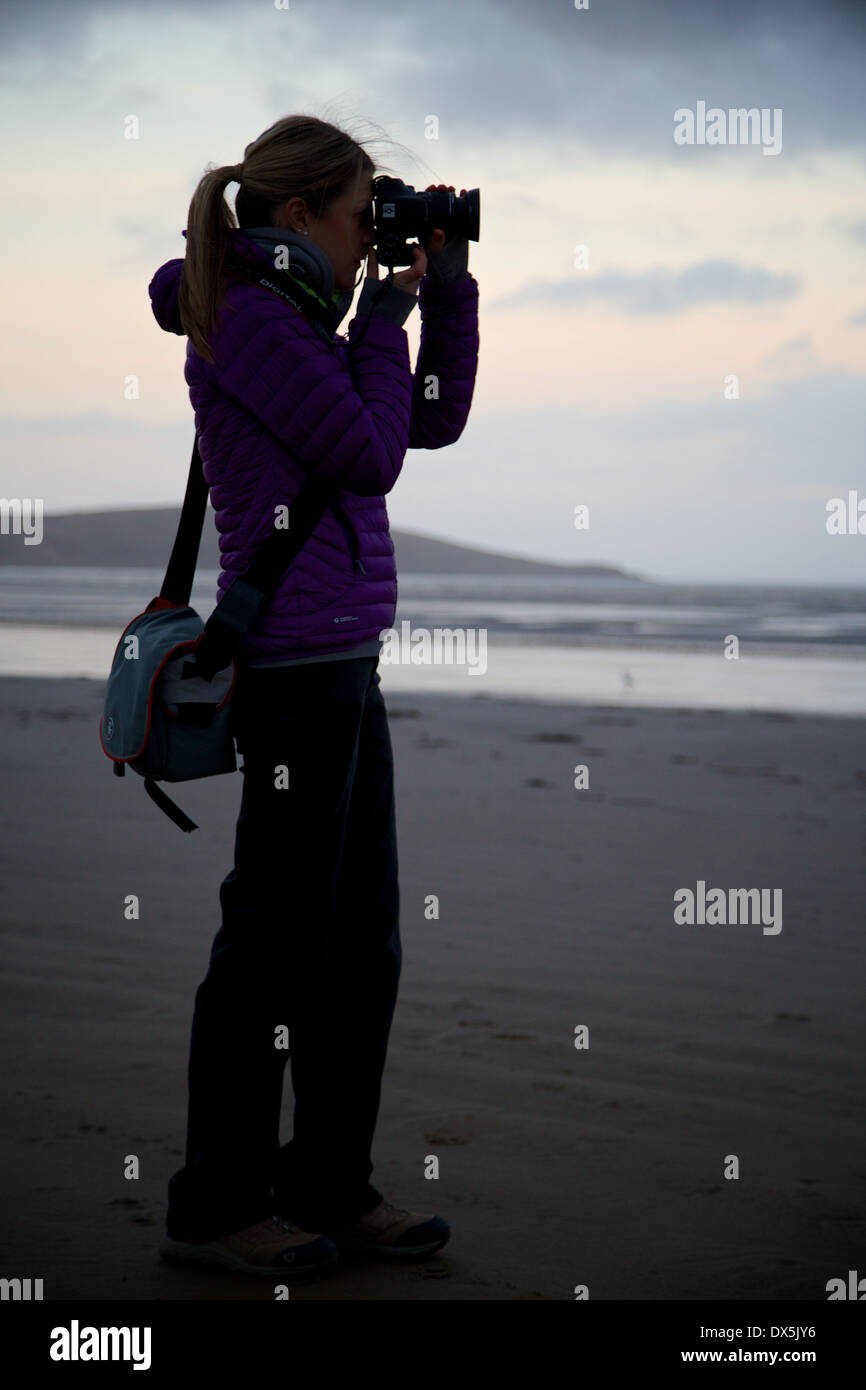 Eine junge Dame, die Aufnahme eines Fotos mit einer DSLR-Kamera an einem Strand in der Dämmerung. Stockfoto