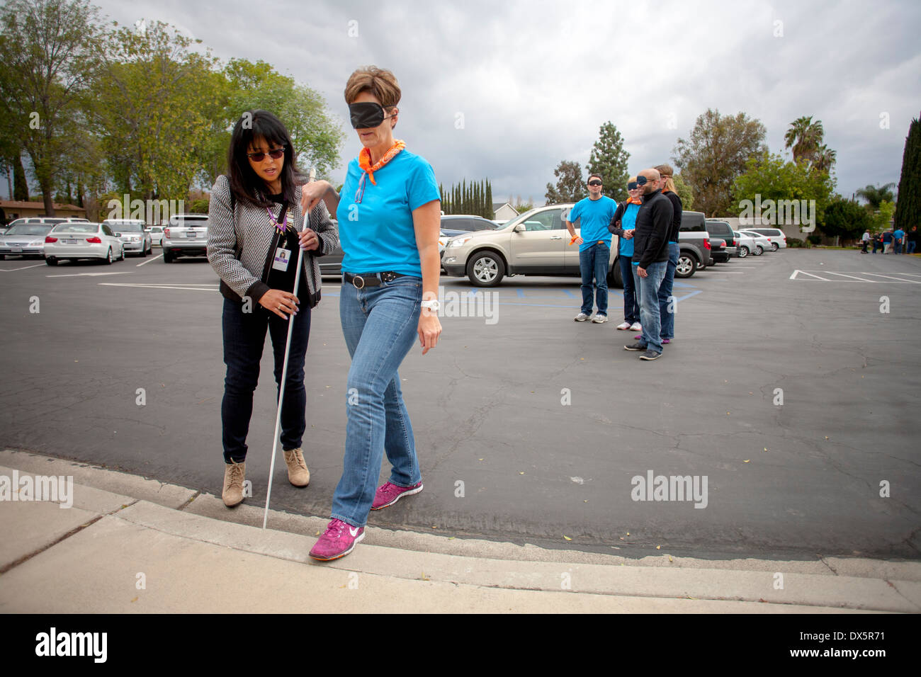 Besucher zu einer Schule für Blinde in Tustin, Kalifornien, werden die Augen verbunden um die es ihnen ermöglichen, Blindheit zu erleben, wie sie lernen, einem Blindenstock zu benutzen, um zu Fuß auf einem Parkplatz. Stockfoto