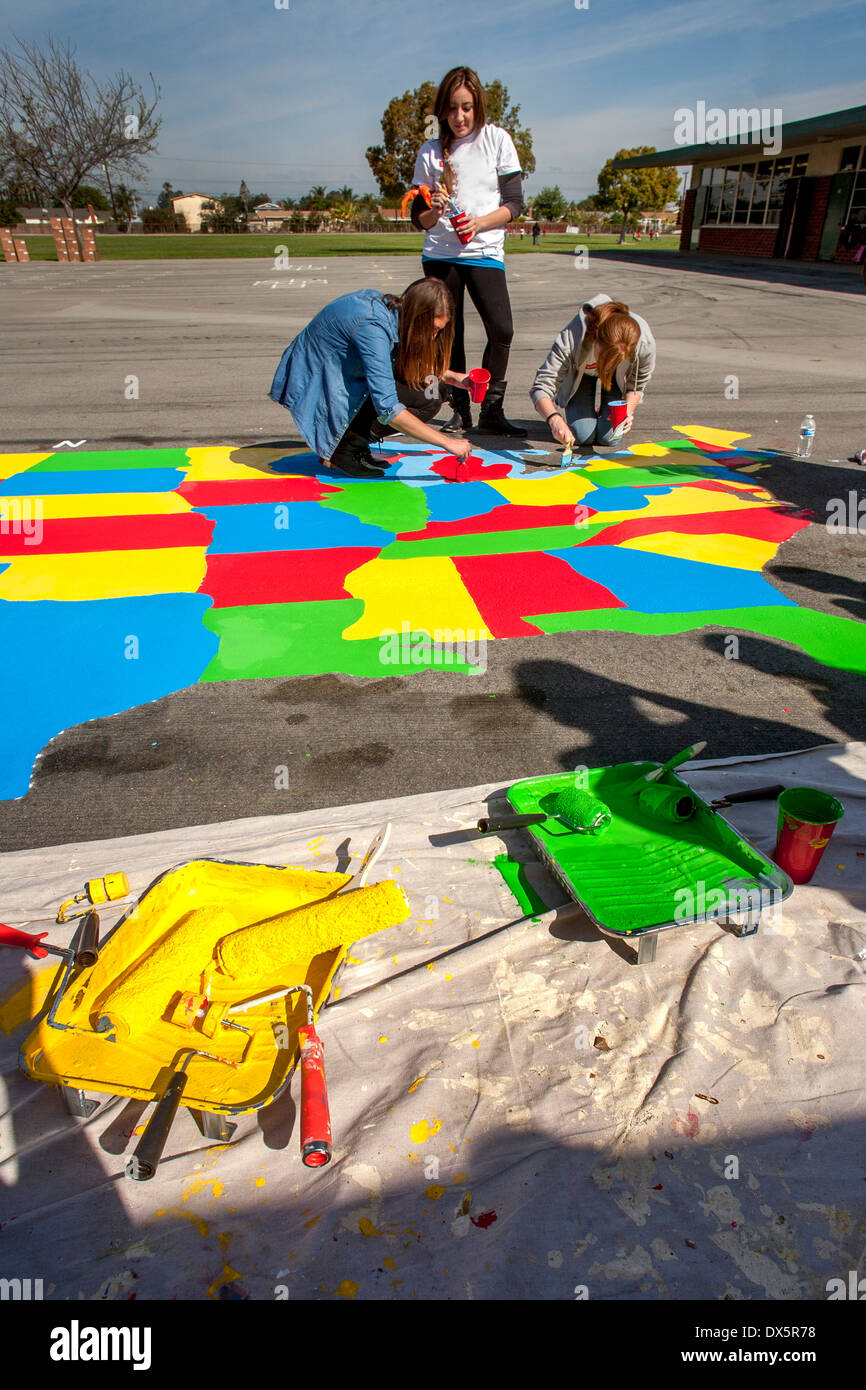 Jungen Erwachsenen ehrenamtlichen Künstler malen eine Karte der Vereinigten Staaten auf einer Grundschule Spielplatz in Garden Grove, CA. Hinweis Malerrollen und Schalen. Stockfoto