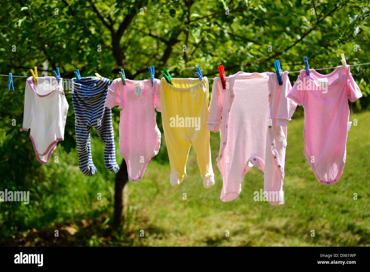 Süße kleine Baby-Kleidung aufhängen auf der Wäscheleine in der Sonne in einer grünen Frühling Garten. Stockfoto