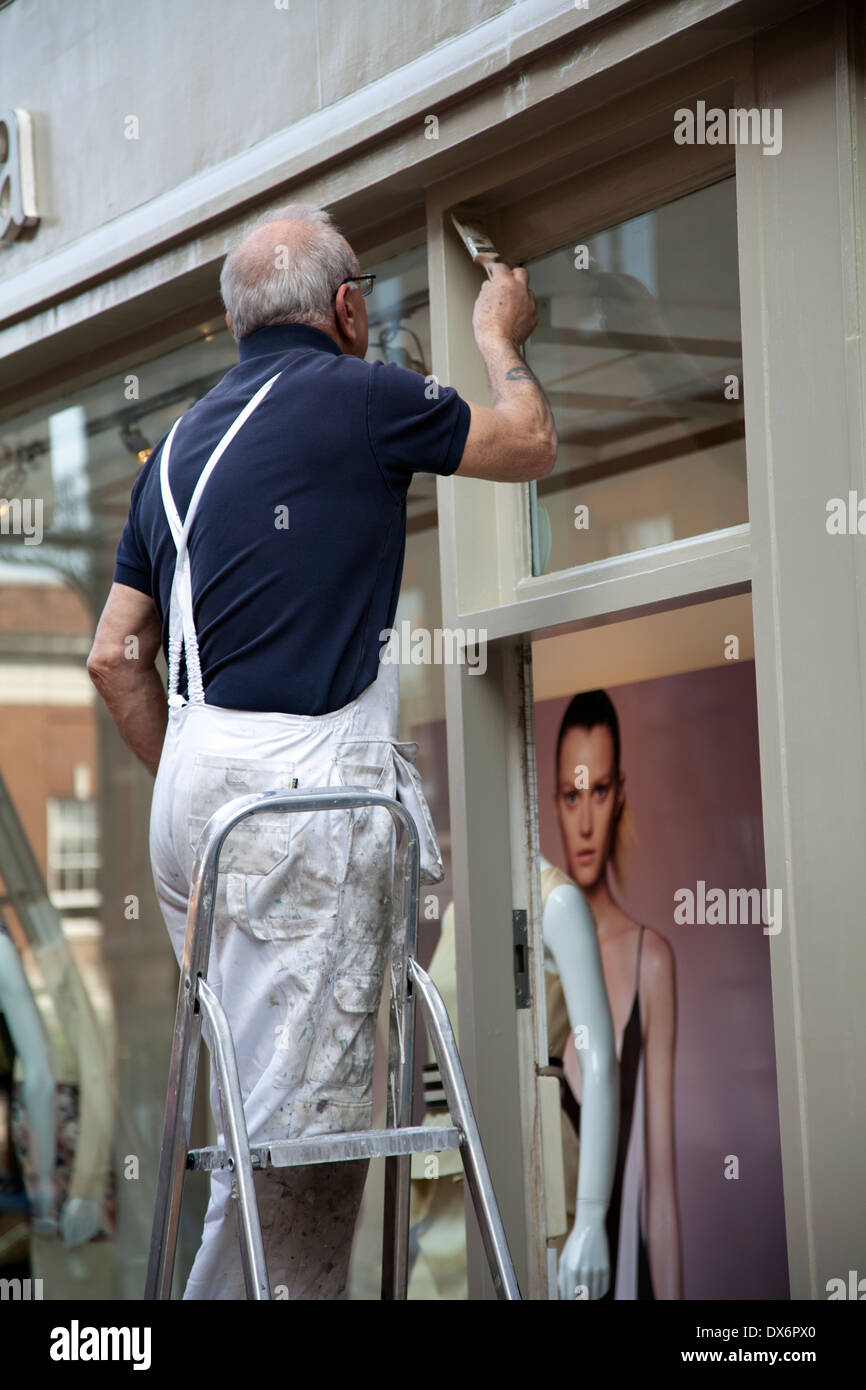 Senior woman auf Leiter Gemälde Shop Tür Rahmen in Richmond London UK Stockfoto