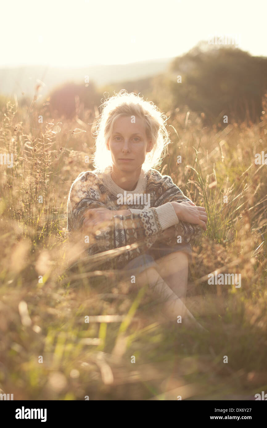 Eine junge Frau sitzt in einem Feld Gras mit der schwindenden dunstige Sonne hinter Stockfoto
