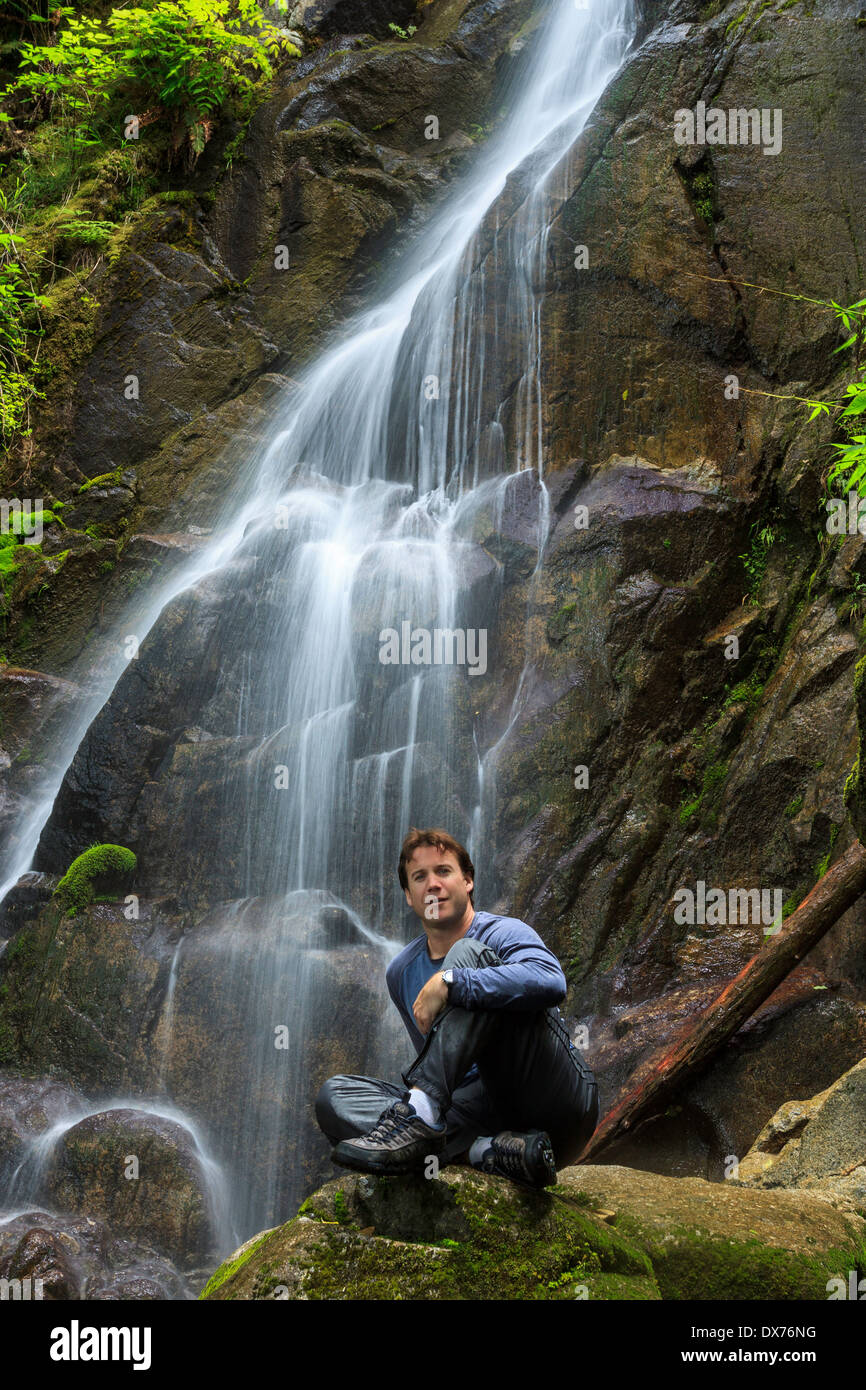 Ein Wanderer entspannt auf einem Felsen vor einem Wasserfall Stockfoto