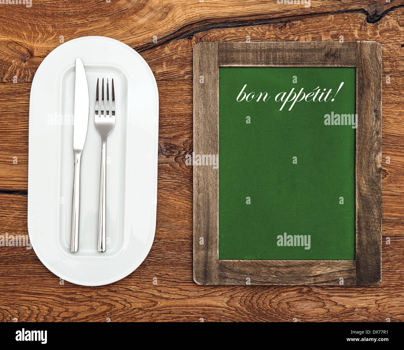 grünen Tafel mit weißen Teller, Messer und Gabel auf Holztisch. Sample Text Bon Appétit! Stockfoto