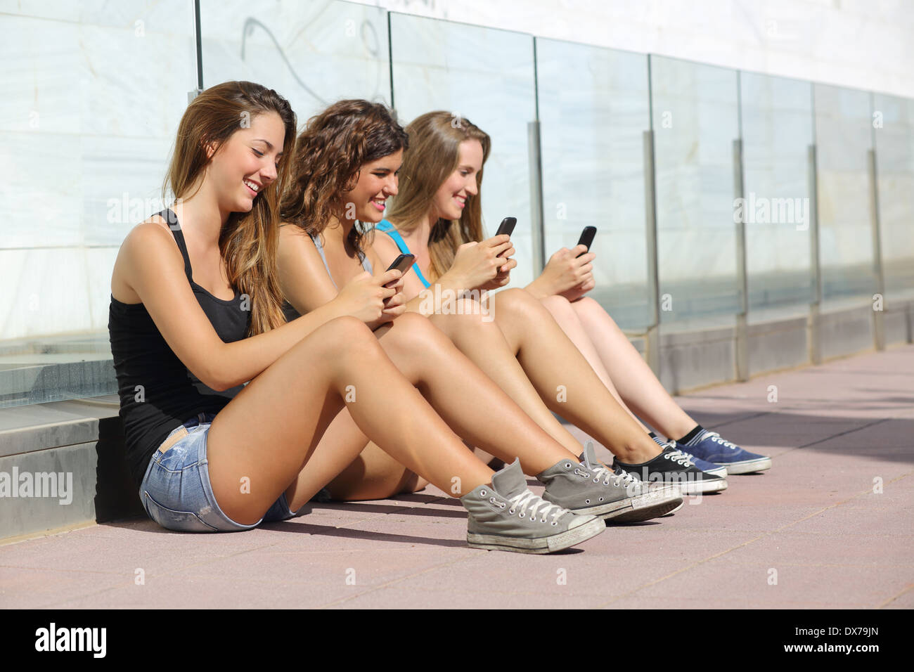 Gruppe von Teenager-Mädchen lächelt glücklich SMS auf dem Smartphone sitzen auf dem Boden im freien Stockfoto