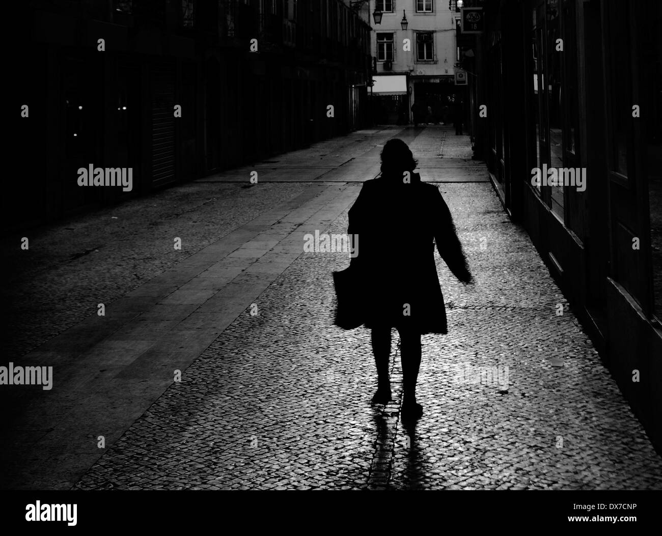 Eine Frau zu Fuß hinunter eine dunkle, stimmungsvolle suchen Straße in Lissabon, Portugal. Stockfoto