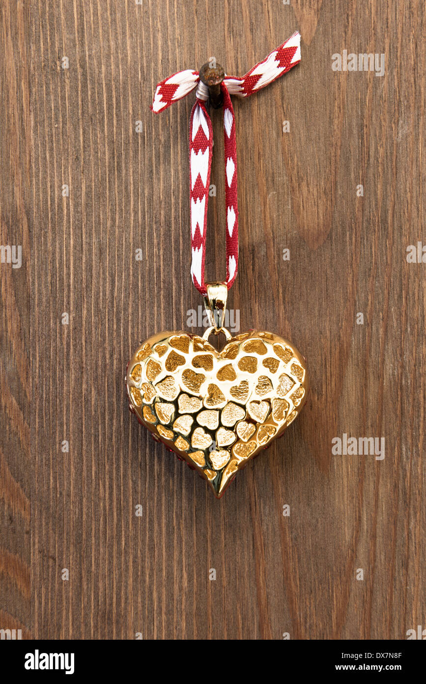 Ein goldenes Herz Ornament durch rote Schleife an einem rostigen Nagel vor einem rustikalen hölzernen Hintergrund hängen. Stockfoto