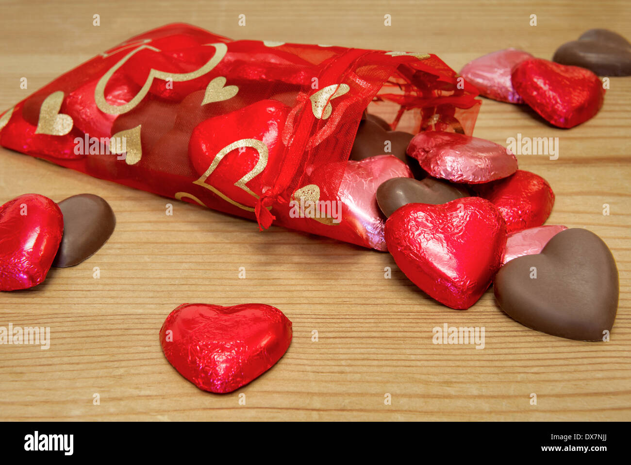 Eine rote Tasche voller Herz geformt Schatz Schokolade auf einem Holztisch verschütten. Stockfoto