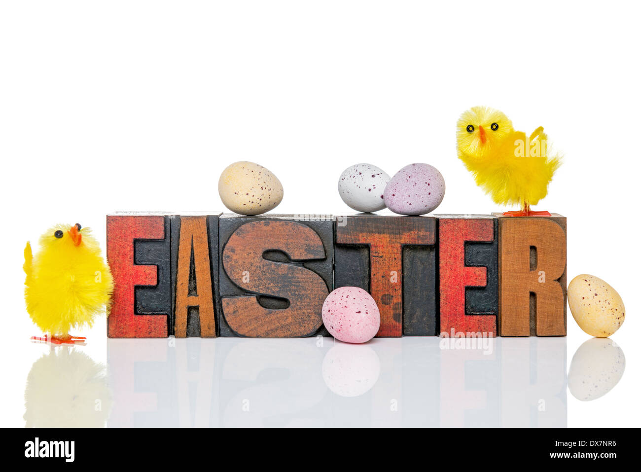 Das Wort Ostern im alten hölzernen Buchdruck mit einem Spielzeug Küken und Süßigkeiten bedeckt Schokoladeneier, isoliert auf einem weißen Hintergrund. Stockfoto