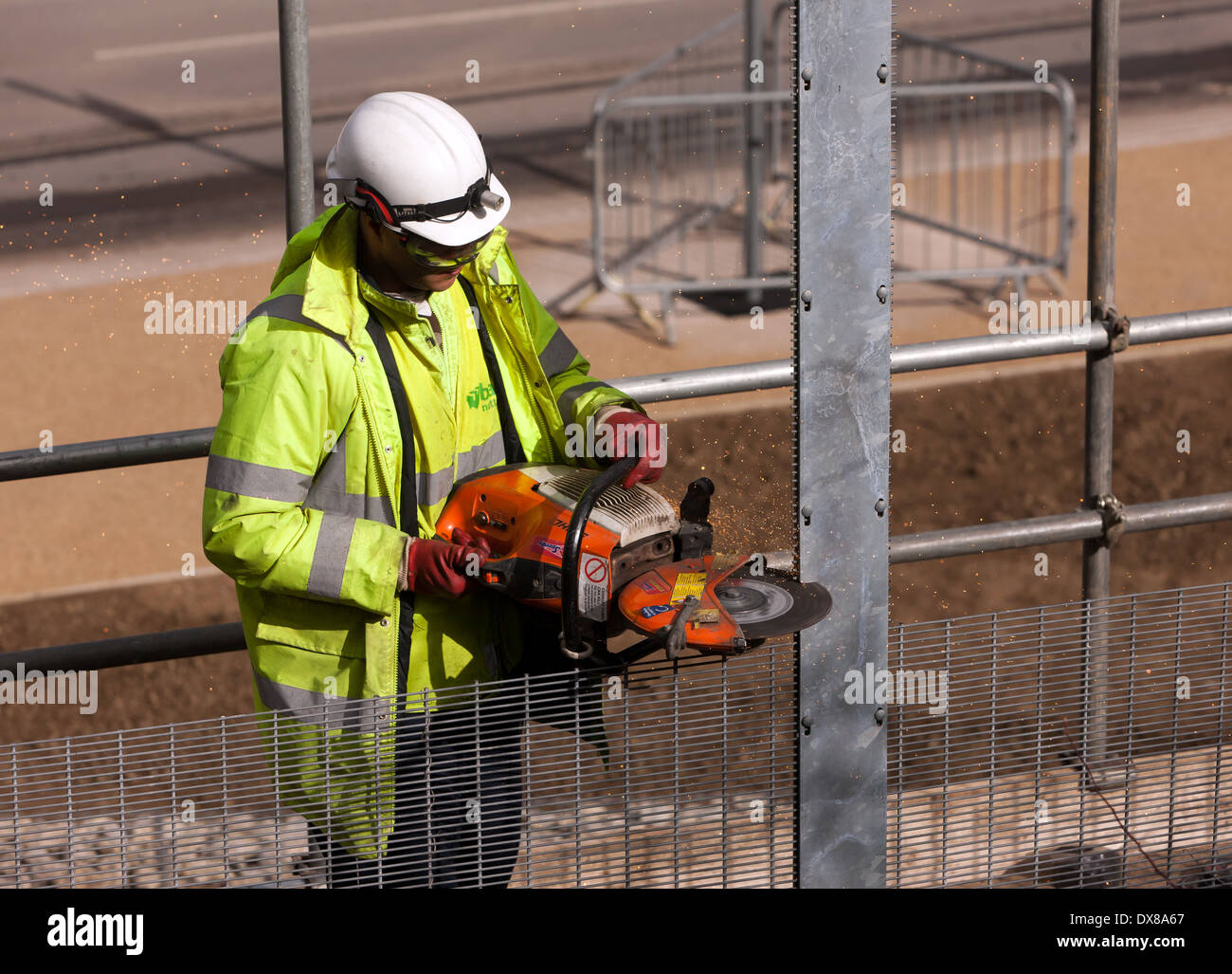 Arbeiter mit einem Winkel-Schleifer, Throughsome Metallzäune an der Queen Elizabeth Olympic Park, Stratford, London zu schneiden. Stockfoto