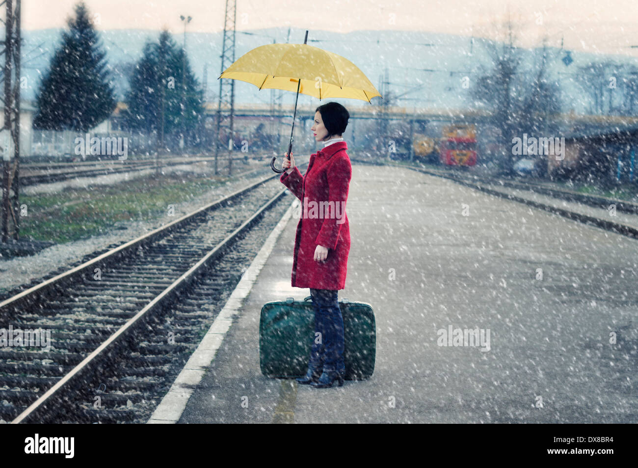 Mitte Erwachsene Frau auf Eisenbahn Bahnsteig mit Koffer hält Regenschirm Stockfoto