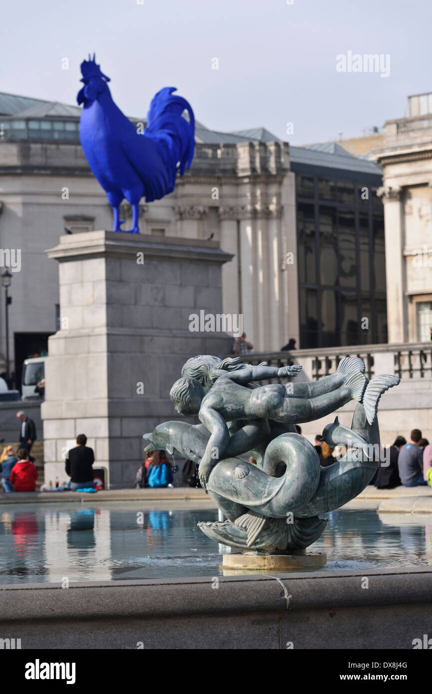 Die Skulptur der Meerjungfrauen und Delfine am Wasserbrunnen mit ein riesiger blauer Hahn im Hintergrund auf dem Trafalgar Square. Stockfoto