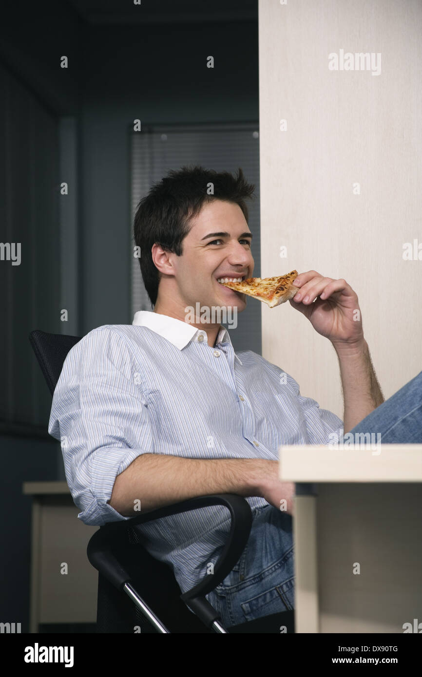 Büroangestellte, Essen ein Pizzastück am Schreibtisch Stockfoto