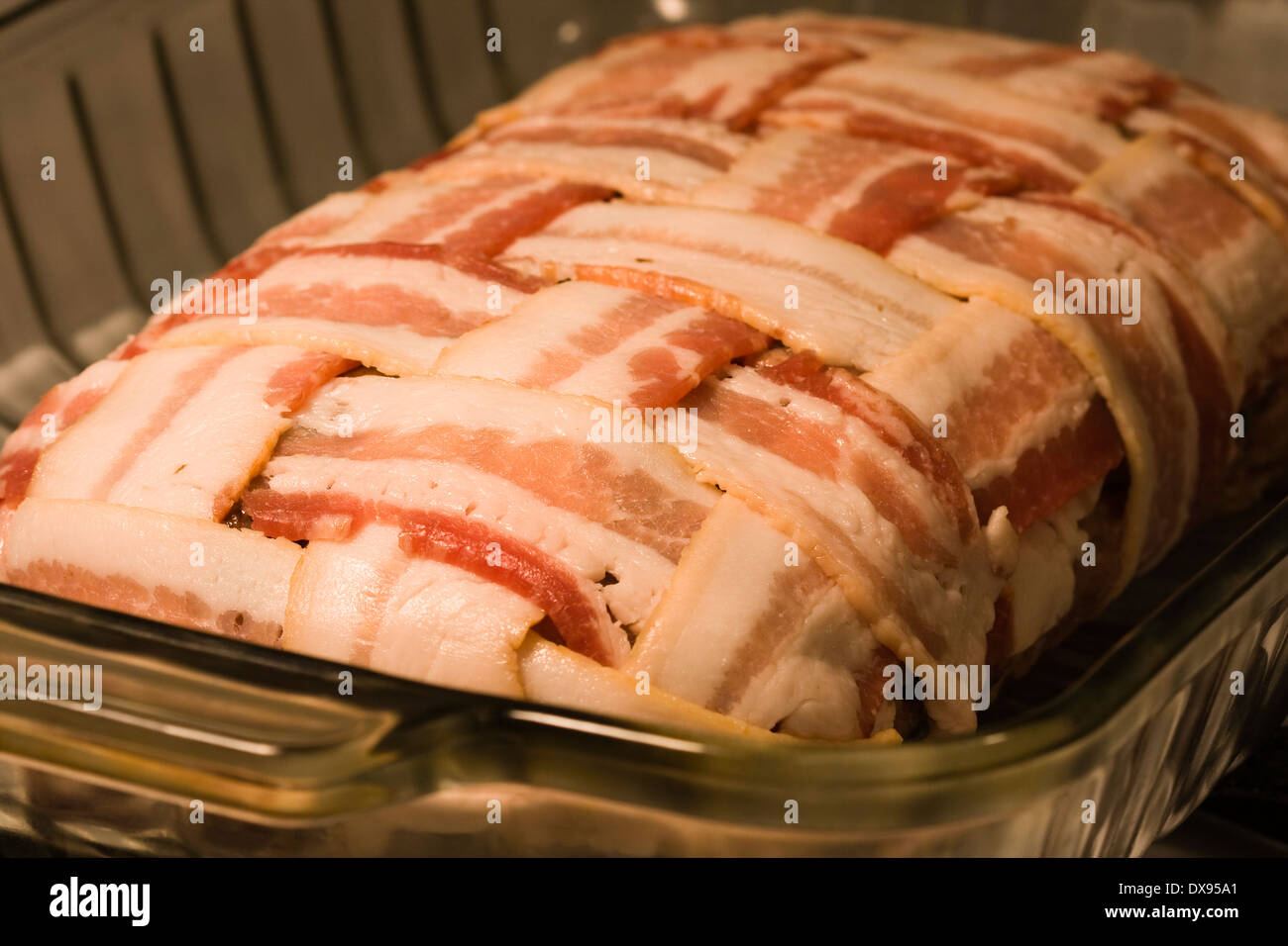 Ungekocht Hackbraten umwickelt mit Speck in einem Korb Flechten Muster sitzen in einer klaren Pyrex Auflaufform auf eine Küche Herd Stockfoto