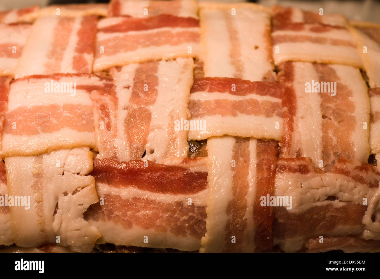 Ungekocht Hackbraten umwickelt mit Speck in einem Korb Flechten Muster sitzen in einer klaren Pyrex Auflaufform auf eine Küche Herd Stockfoto