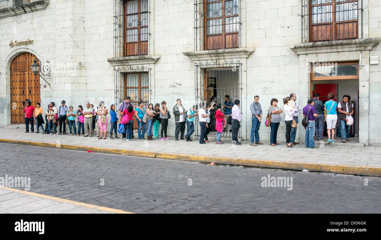 langen Reihe von unterschiedlichsten Menschen warten auf Geldautomaten Bargeld benutzen erstreckt sich auf Bürgersteig außerhalb Santander Bank Oaxaca Stockfoto