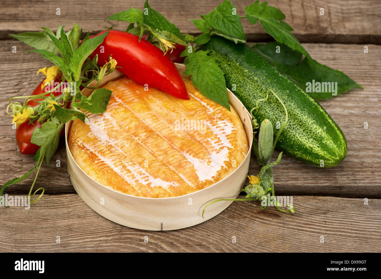 Gebackener Camembert Käse mit frischem Gemüse. Tomaten und Gurken mit Blättern und Blüten über rustikale Holz Hintergrund Stockfoto