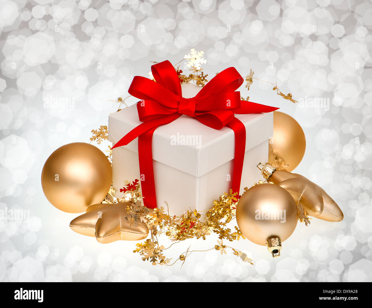 weißen Geschenkbox mit roter Schleife und goldene Kugeln Dekoration über der Hintergrund jedoch unscharf Stockfoto