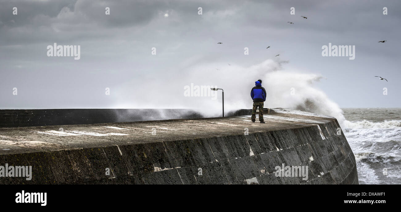 Eine einsame Person, die Wellen brechen gegen eine Hafenmauer zu beobachten Stockfoto