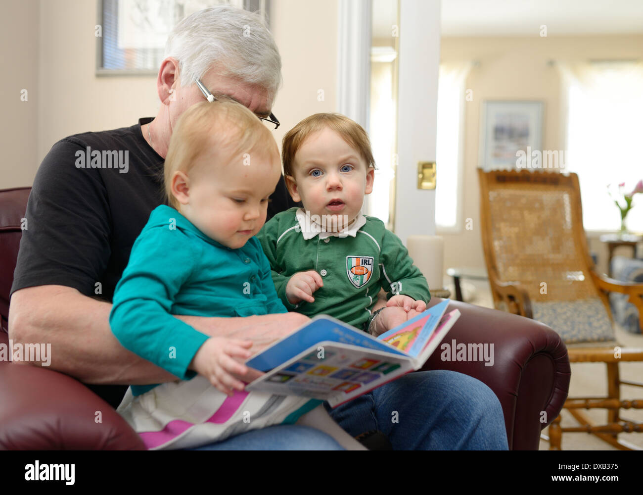 Jungen und Mädchen Zwillingskinder auf Großväter Schoß ein Geschichte Buch zu Hause Stockfoto