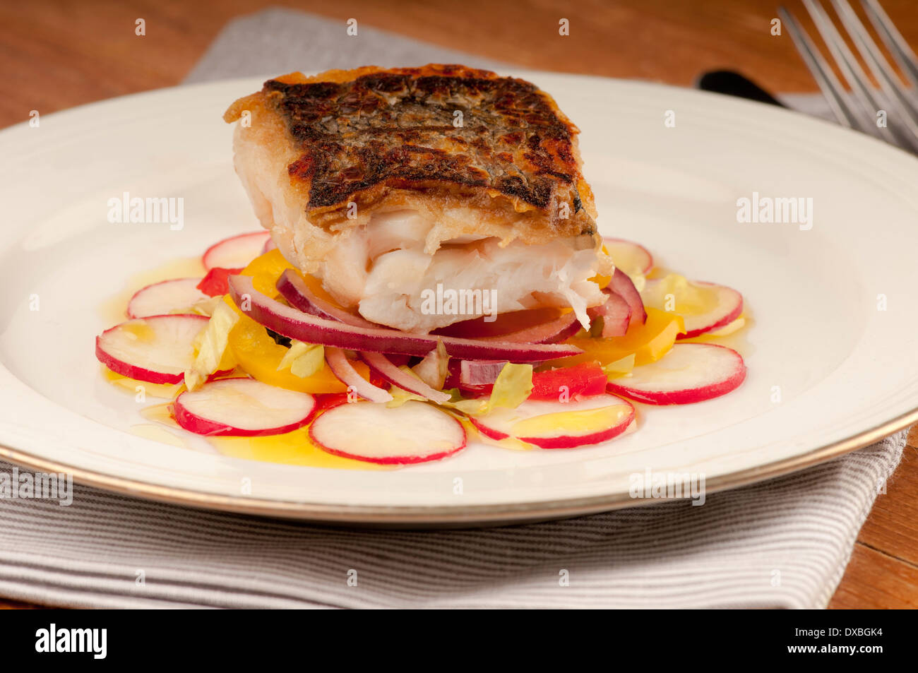 Knusprig gebratene Kabeljaufilet auf einem Bett aus Rettich und rote Zwiebel auf einem weißen Teller Stockfoto