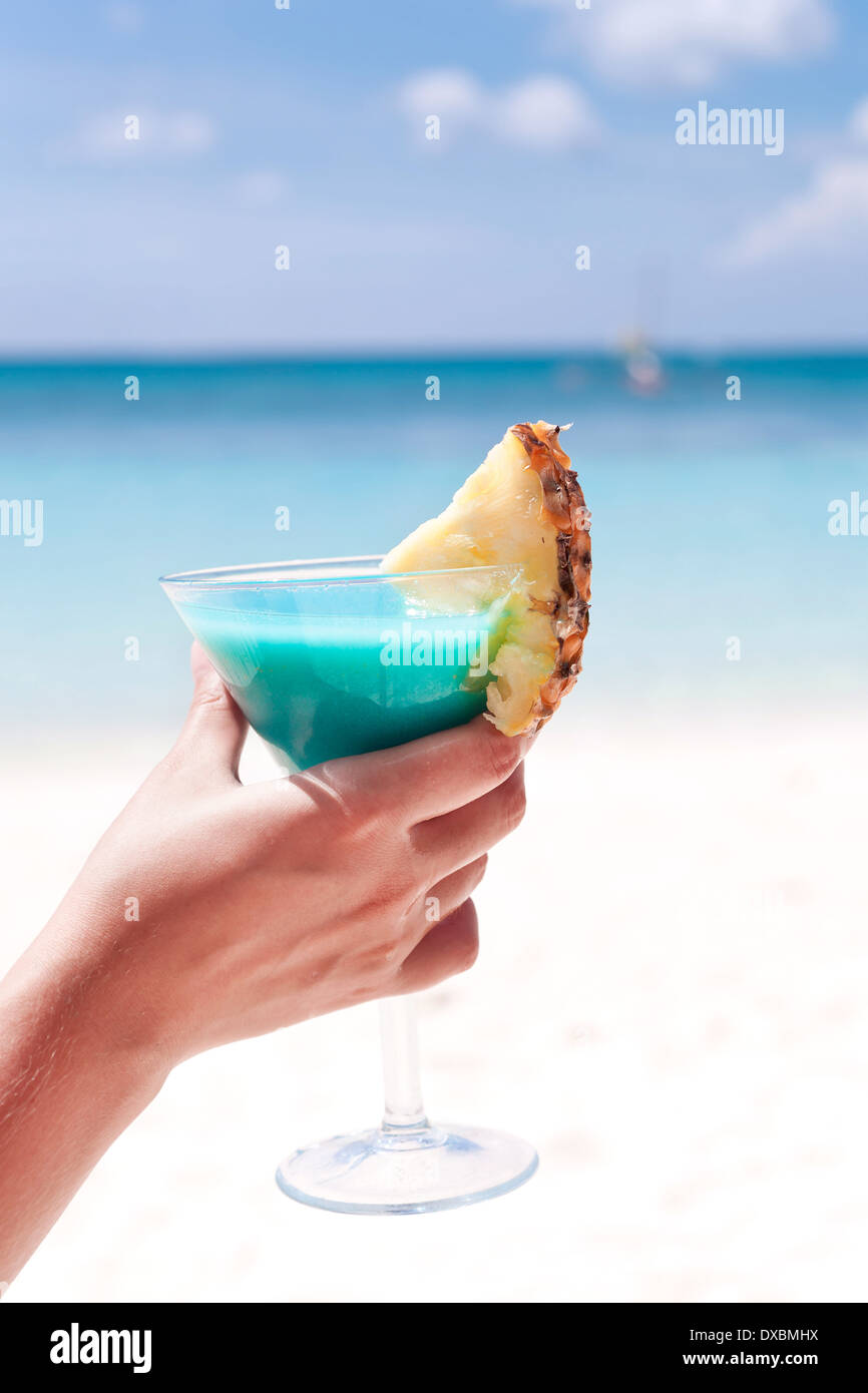 Blue Curacao cocktail mit Scheibe Ananas am weißen Strand in weiblicher hand Stockfoto