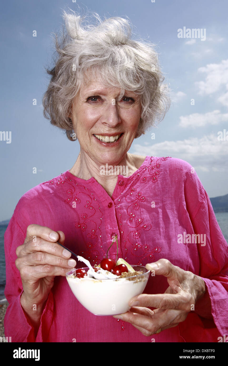 Weibliche Senior Essen Joghurt und Obst am Strand Stockfoto