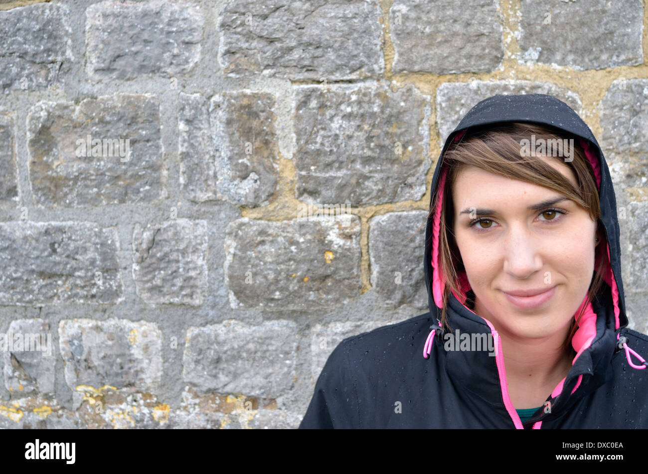 Brunet Mädchen Lächeln auf den Lippen tragen eine Kapuze gegen Steinmauer Stockfoto