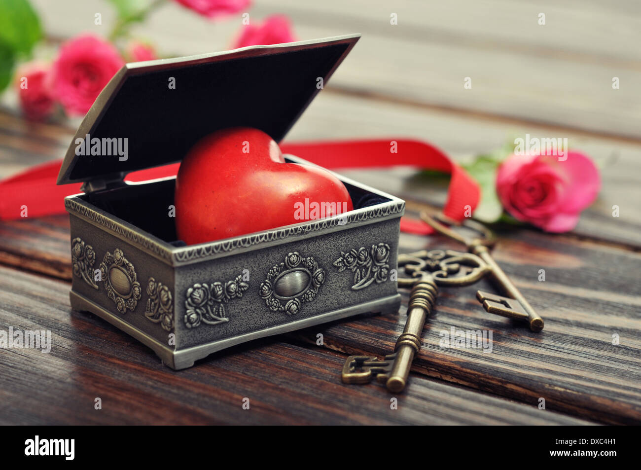 Das steinerne Herz in Vintage Zinn Geschenkbox mit Schlüssel und Rosen auf hölzernen Hintergrund Stockfoto