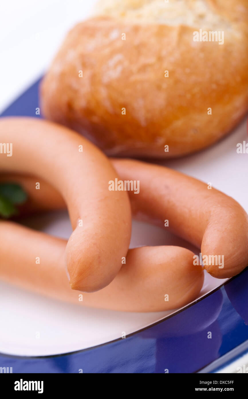 Drei kalt geräucherte Würstchen oder Wiener Würstchen serviert auf einem Teller mit einem Sprung in eine kleine Schüssel geben und in Scheiben geschnittenen Kirschtomaten auf ein weißes Studio-Hintergrund Stockfoto