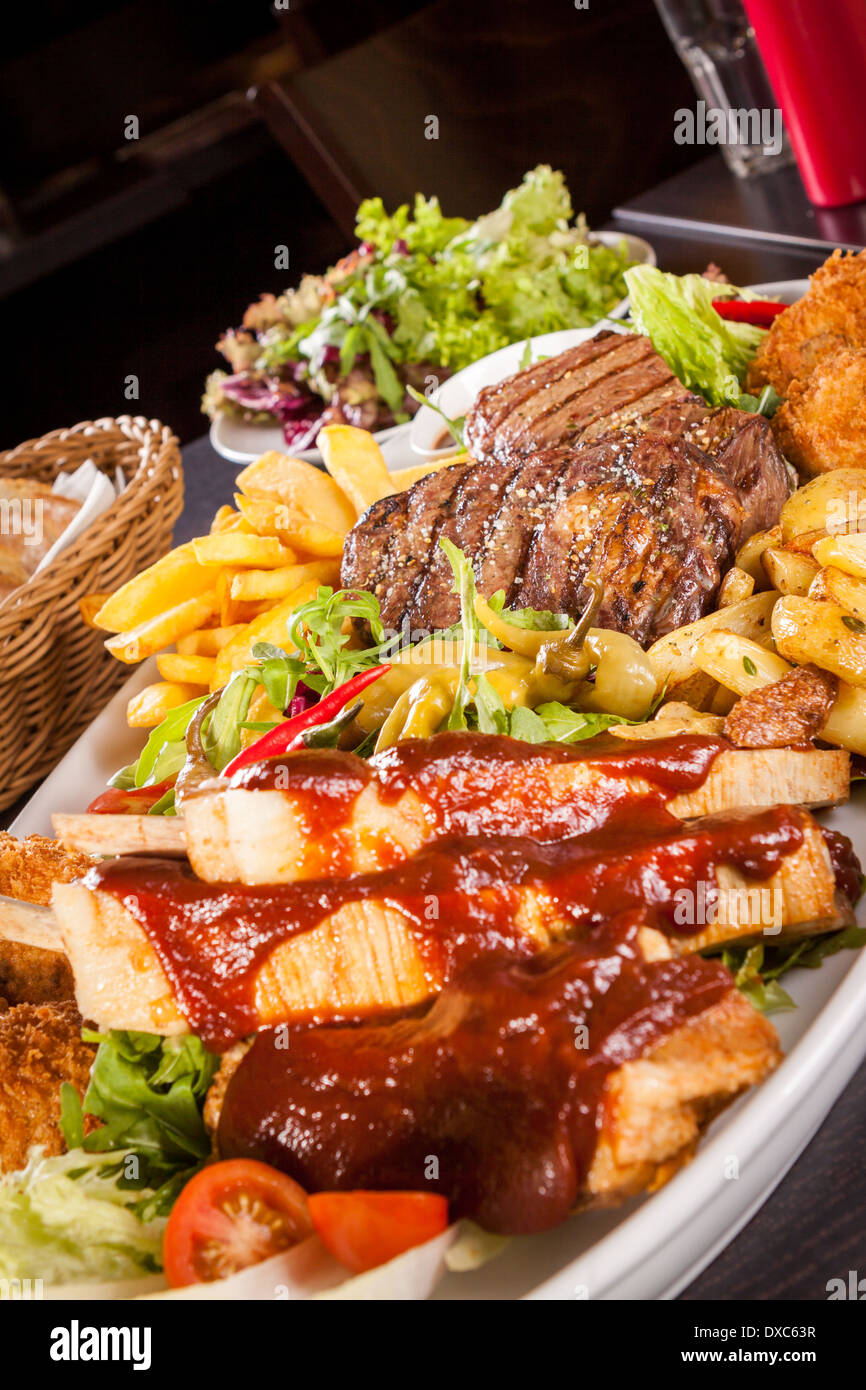 Gesunde Platte mit gemischtem Fleisch einschließlich gegrilltes Steak, knusprig Panierter Hühner- und Rindfleisch auf einem Bett aus frischen grünen grün gemischter Salat serviert mit Pommes Frites und Chutney oder BBQ-Sauce in eine Schüssel Stockfoto
