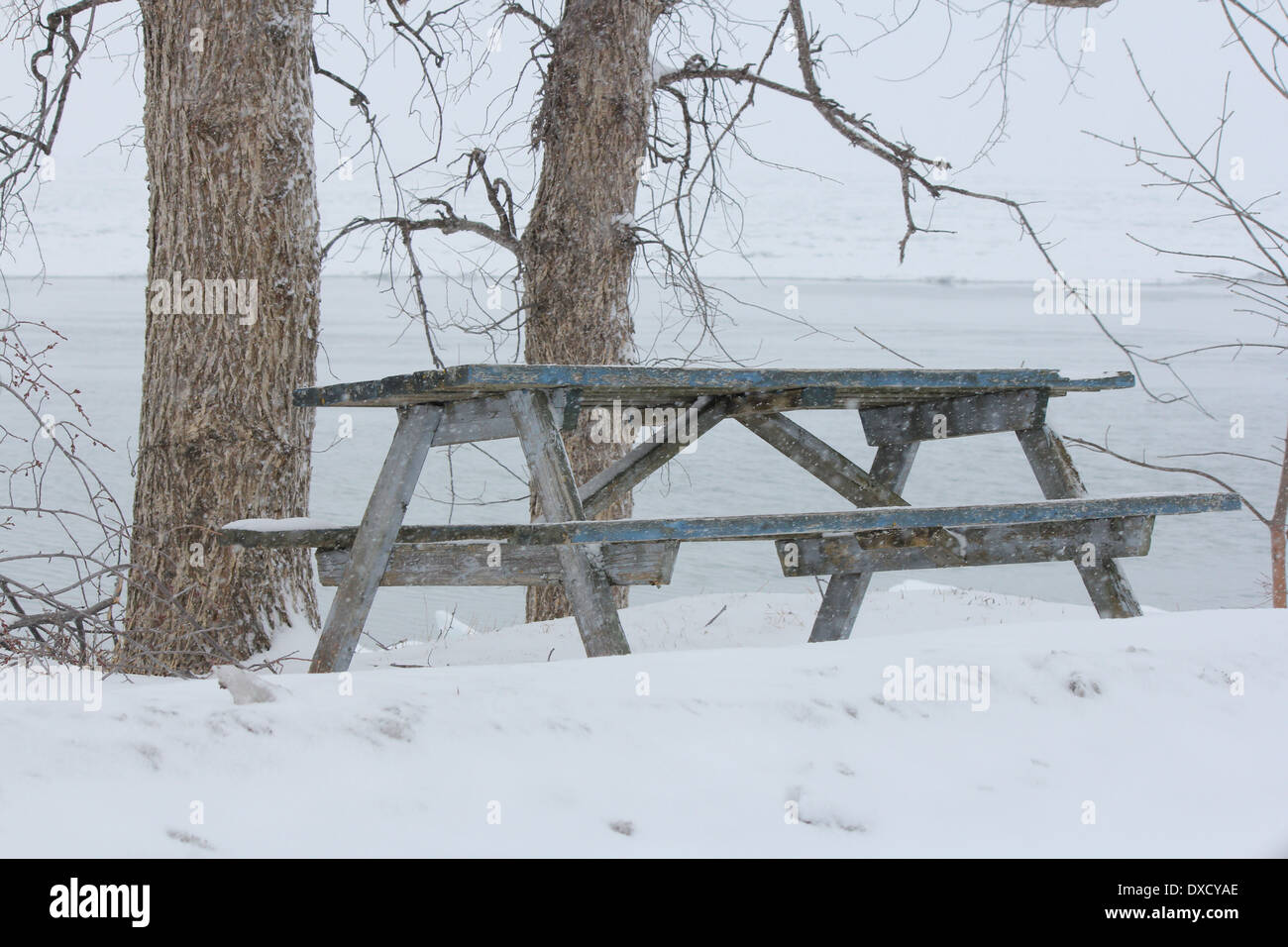 Eine leere Picknick-Tisch auf einer verschneiten Anhöhe mit Blick auf einem zugefrorenen See. Stockfoto