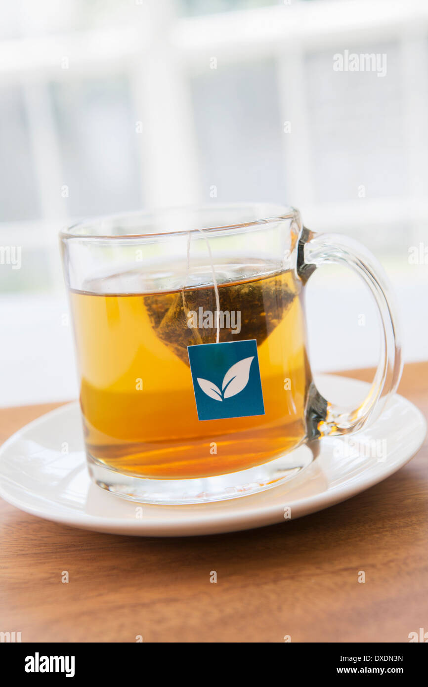 Tasse Tee im klaren Becher mit Pyramid Teebeutel und blauen Tag auf Holztablett, Studioaufnahme Stockfoto