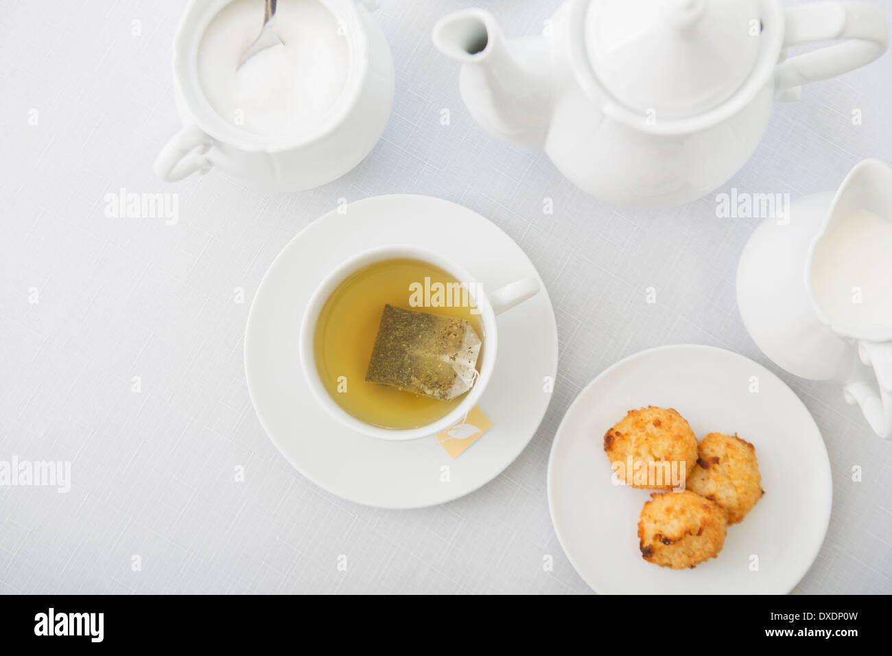 Tasse Tee in weißem Porzellan Teetasse mit Unterteller, Zuckerdose, Milchkännchen, Teekanne und Teller Kokosmakronen, Studio gedreht Stockfoto