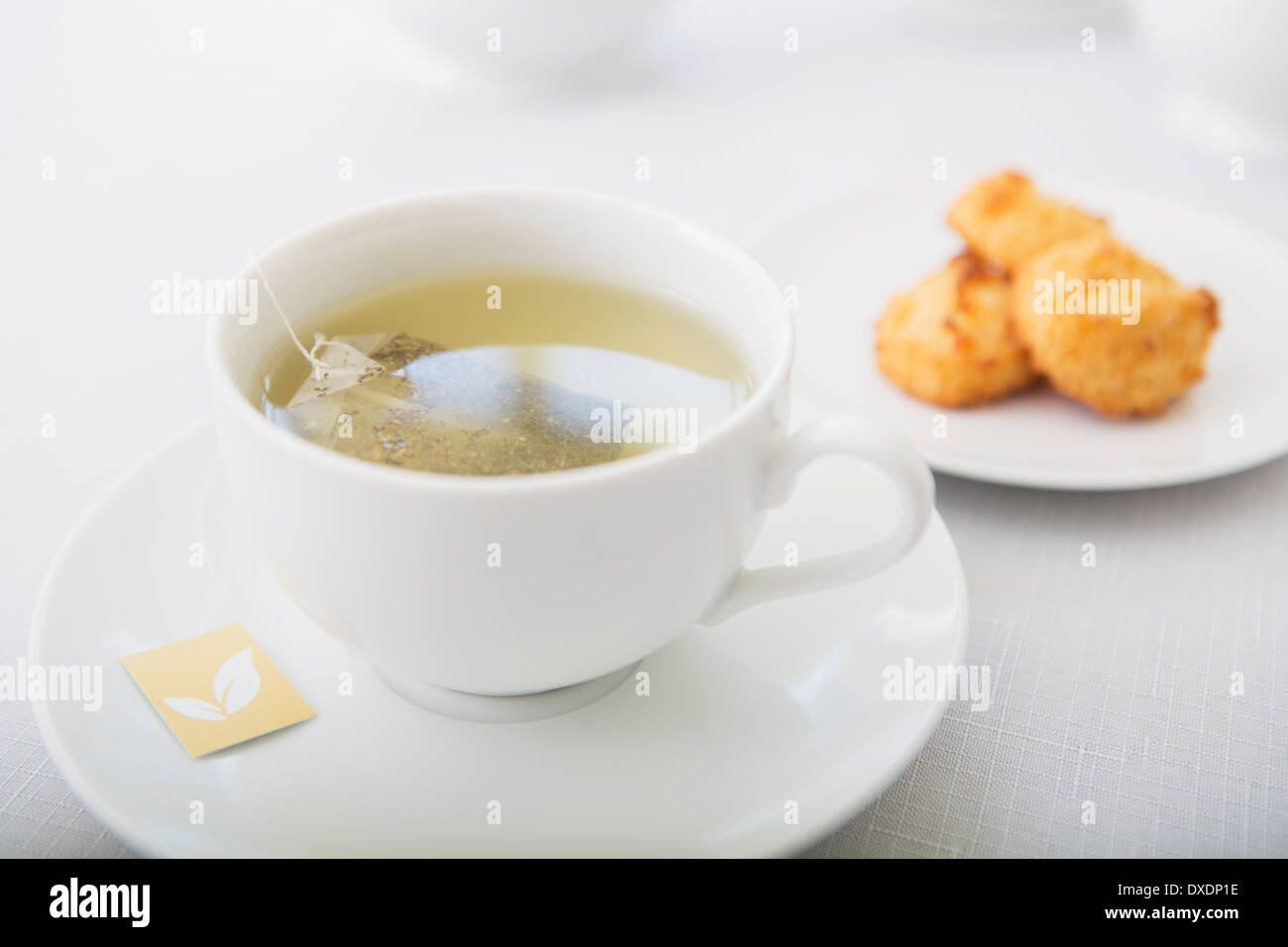Tasse Tee in weißem Porzellan Teetasse mit Untertasse und Teller mit Kokosmakronen, Studio gedreht Stockfoto