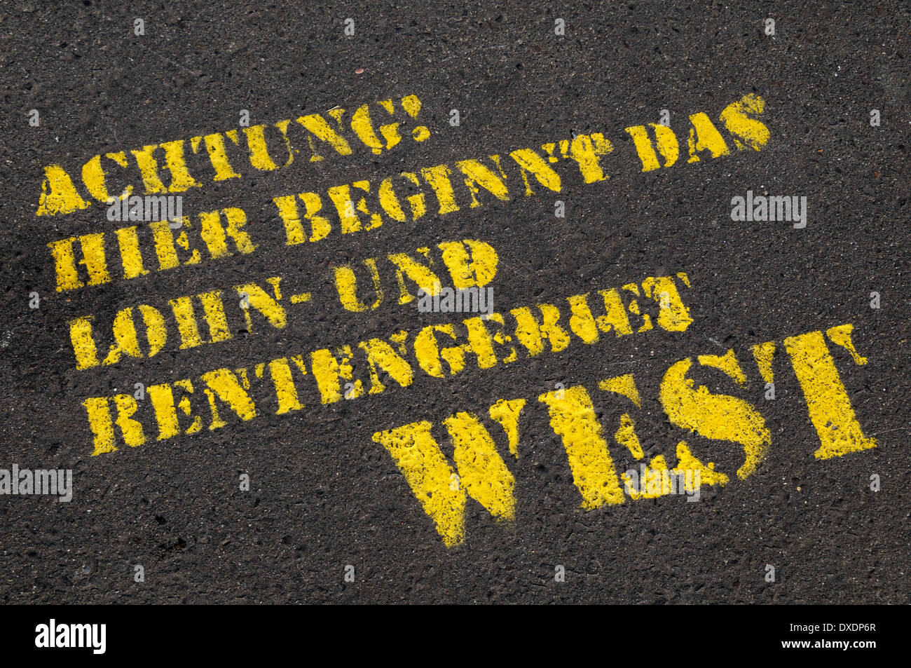 Nahaufnahme der deutsche Text auf asphaltierten Straße (Achtung, hier beginnt der Bereich der Lohn- und Rentenkürzungen West), Berlin, Deutschland Stockfoto