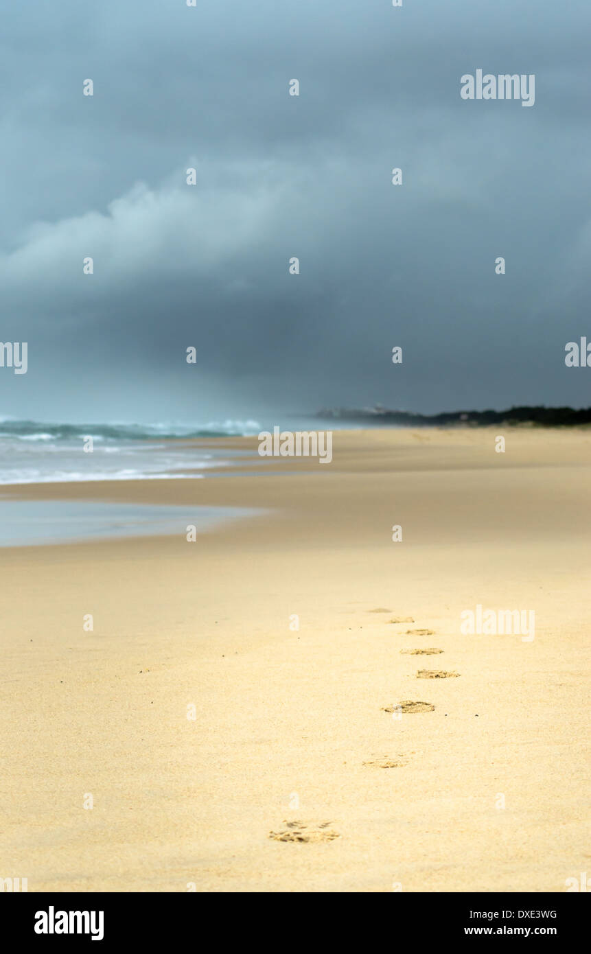 Fußspuren im Sand führen das Auge in einer dunklen bedrohlichen Himmel über den Strand vor. Stockfoto