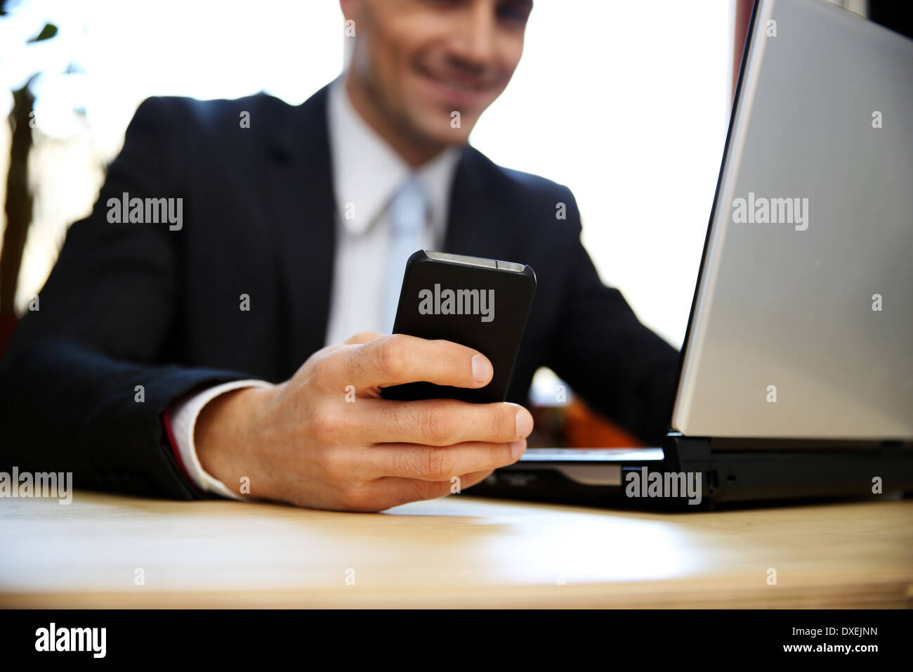 Geschäftsmann mit Laptop und Smartphone im Büro. Fokus auf Smartphone. Stockfoto