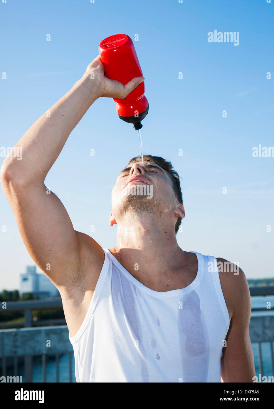 Junge Mann gießt Wasser aus Wasserflasche auf seinem Gesicht, Worms, Rheinland-Pfalz, Deutschland Stockfoto