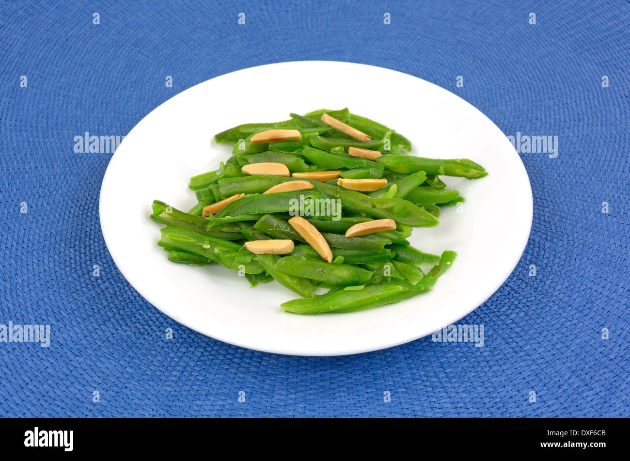 Eine kleine Portion grüne Bohnen mit Mandelsplitter auf einem weißen Teller oben auf einer blauen gewebte Platzdeckchen. Stockfoto