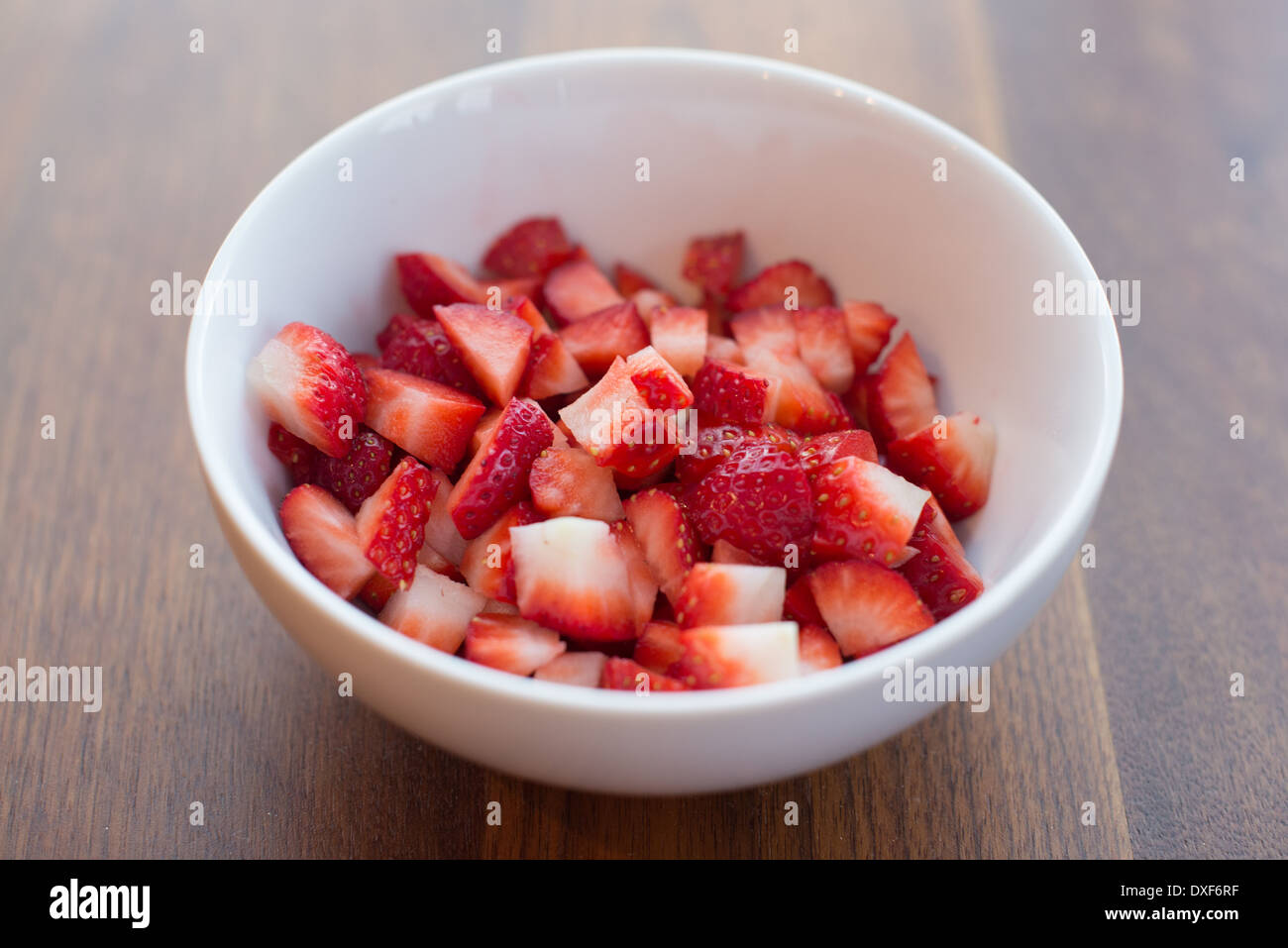 Frische Erdbeeren in Scheiben geschnitten in einer weißen Schüssel auf einem Holztisch Stockfoto