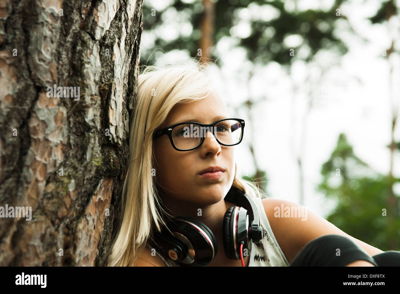 Close-up Portrait von Mädchen tragen Brillen, sitzen neben Baum im Park, mit Kopfhörern um Hals, Deutschland Stockfoto